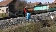 Baba baca smeće na travu pored pruge